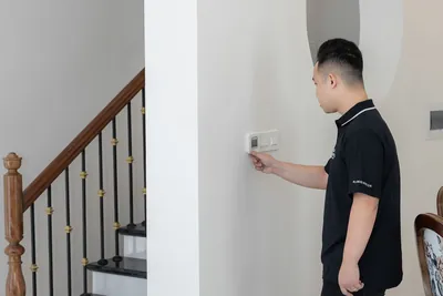 A young man adjusting a thermostat on an indoor wall