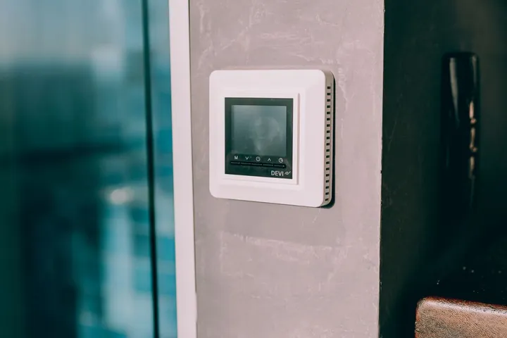 A smart thermostat mounted on a concrete wall in a modern interior