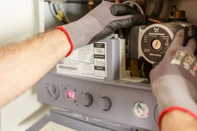 A technician's gloved hands adjusting the controls on a home heating unit during service
