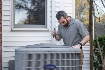 A technician calmly inspecting an outdoor HVAC unit beside a house