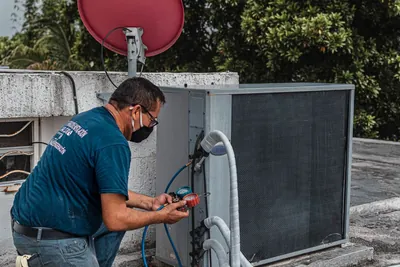 A technician wearing a facemask diagnosing an air conditioning unit with a manifold gauge