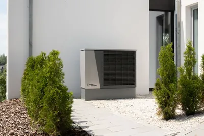 An outdoor air conditioning unit beside a modern house, surrounded by landscaping